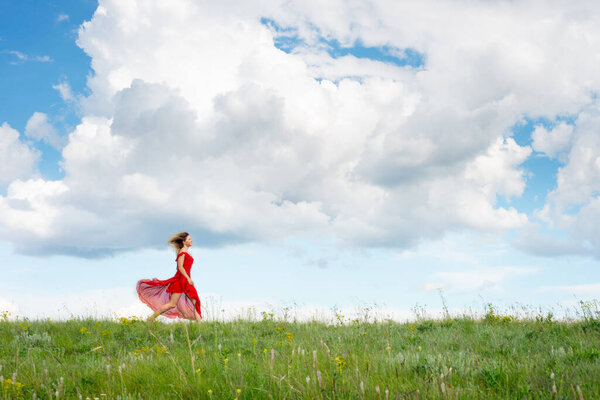 Beautiful happy woman in red dress runs on a green field