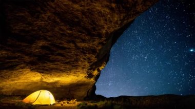 Parıldayan yıldızlı gökyüzünün altında gece mağarasında parlayan bir kamp çadırı. Sinemagraf