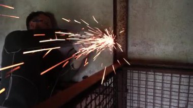 Öğütücü kullanan işçi bir atölyede metal kesiyor.