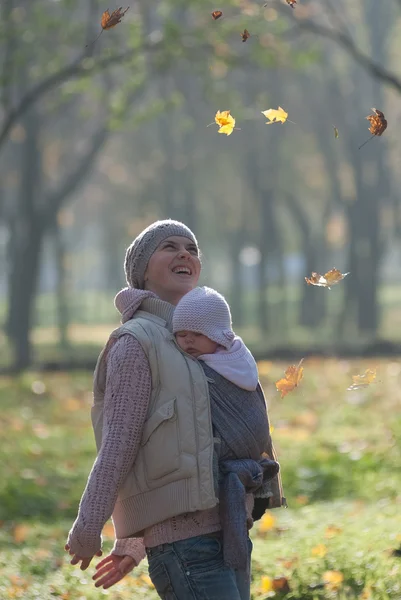 Maminka a miminko v šátku radovat padající listí — Stock fotografie