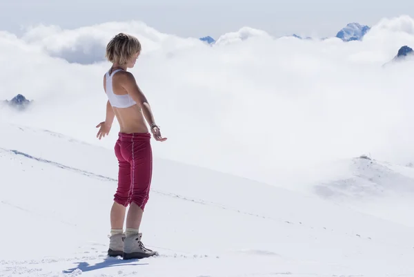 Blonde meisje in de besneeuwde bergen hoog boven de wolken — Stockfoto