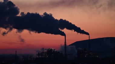 Fabrika borularından gelen duman günbatımı gökyüzünün arka planında.