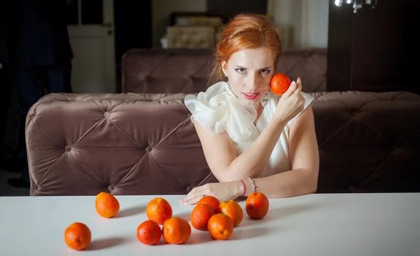 Schöne rothaarige Mädchen mit Mandarinen im weißen Kleid — Stockfoto