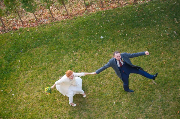 Novia y novio caminando sobre la hierba verde tomados de la mano y riendo —  Fotos de Stock