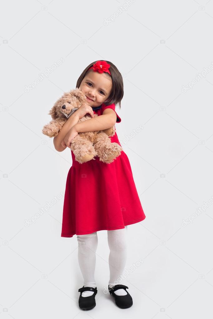 Beautiful smiling little girl in a red dress with a toy bear