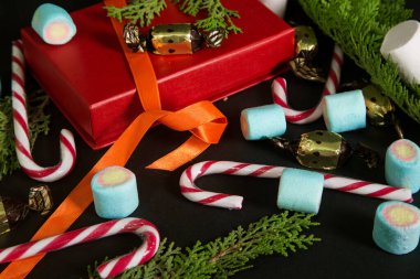 Kırmızı hediye kutusu, şeker kamışı ve siyah arka planda lokum. Noel fotoğrafı, yeni yıl arkaplanı