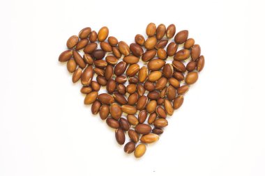 Beyaz bir zemin üzerinde Argan ağacı fındığı olan Argania spinosa kalp şeklinde serilmiş. Argan yağı üretimi için