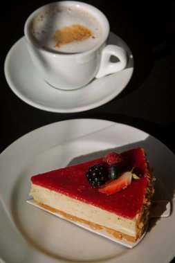 Vanilyalı cheesecake ve arka planda bir fincan kapuçino.