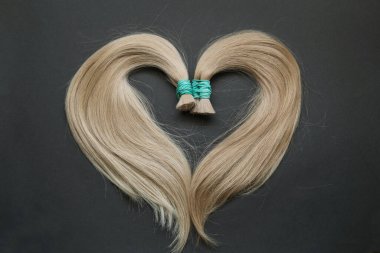 Genişleme için saç telleri koyu bir arka planda kalp şeklinde dizilmiş. Yüksek kalite fotoğraf