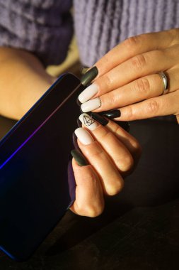 Cep telefonu güzel siyah beyaz manikürlü genç bir kadının elinde. Yüksek kalite fotoğraf