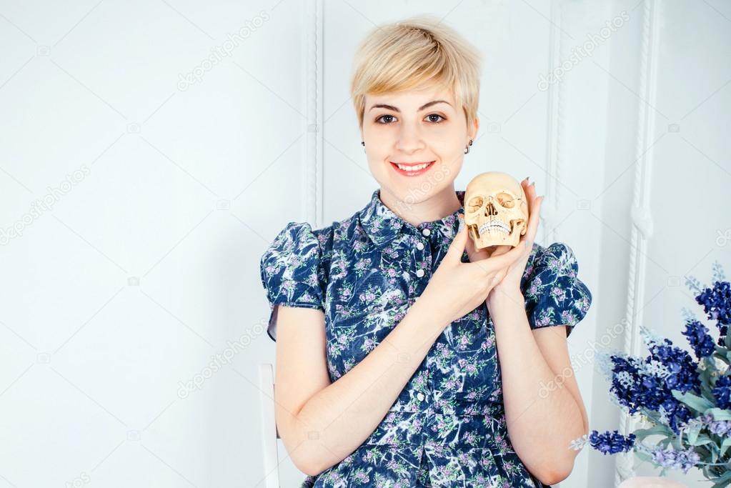 Portrait of a smilling beautiful blonde girl holding skull