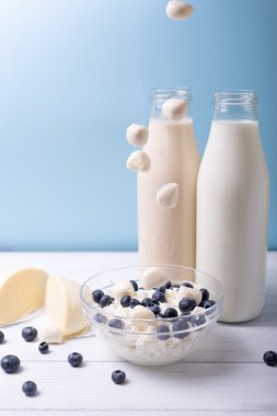 Yaz kahvaltı. Yaban mersini ve süt ürünleri düşen düşen grup ile mavi arka plan ile ahşap bir beyaz masa üzerinde mozzarella. Dikey vurdu. 