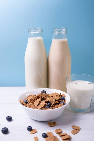 Frühstück mit Milch und Getreide mit Blaubeeren und Flaschen auf einem hölzernen weißen Tisch. Senkrechtschuss — Stockfoto