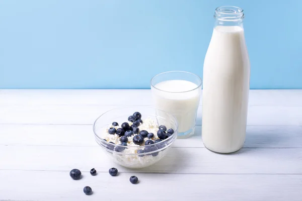 Frische Blaubeeren und Milchprodukte auf weißem Holztisch vor blauem Hintergrund. mit zentralem Fokus und geringer Schärfentiefe — Stockfoto