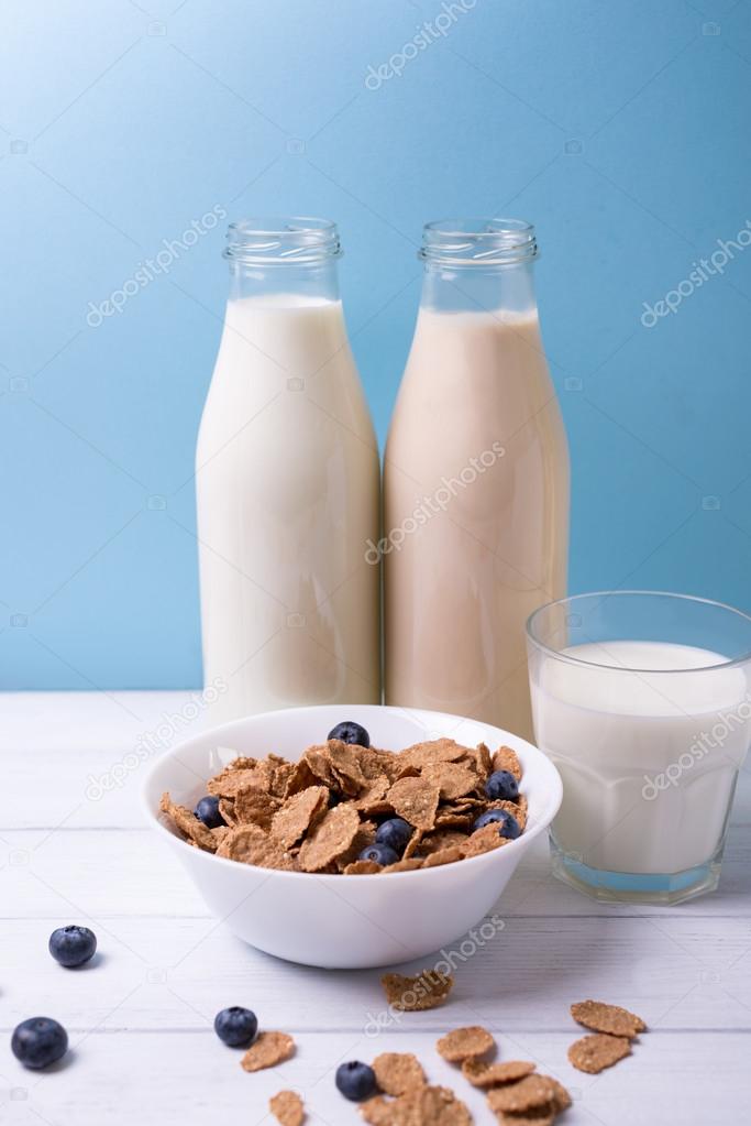 Breakfast with milk and cereals with blueberries with bottles on a background on a wooden white table. Vertical shot