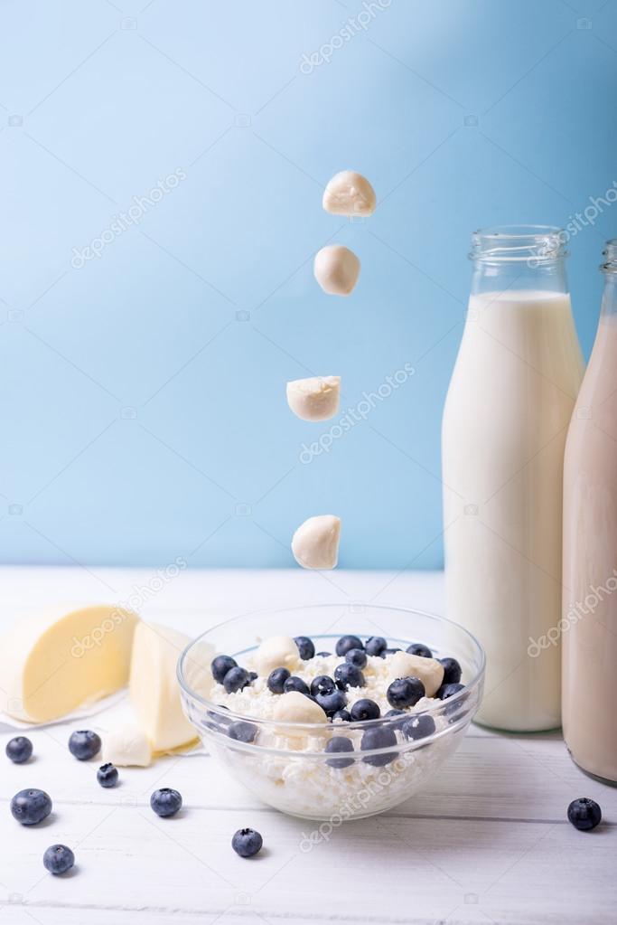 Summer breakfast. Blueberry and dairy products with alternately  falling mozzarella on a wooden white table with blue background. Vertical shot. 