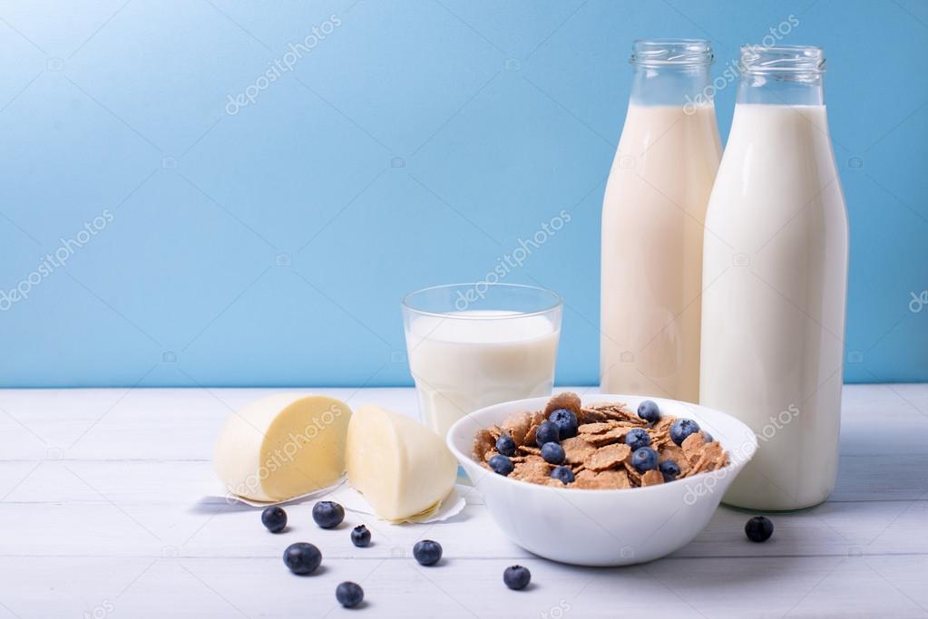 Front view of fresh dairy products and cereals with blueberries on a white wooden table and blue background. Shallow depth of field