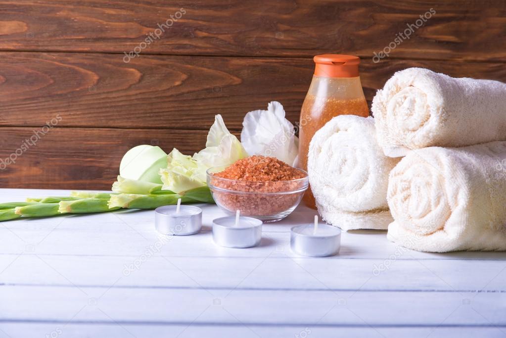 Spa setting with natural olive bath boamb, sea salt, scrub, flowers, towels and candles. On a white wooden table. with copy space.