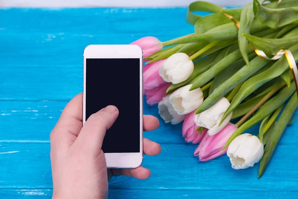 Hombre mano celebración de teléfono inteligente contra tulipanes primavera —  Fotos de Stock