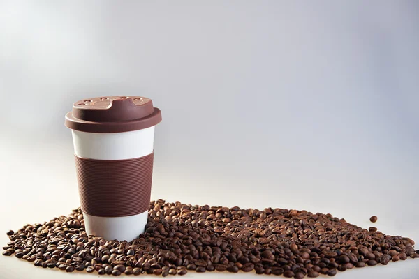 Takeaway ceramic cup and coffee beans on blue background