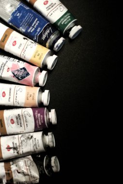 Farklı renklerde yağlı boya tüpleri zıt siyah arka planda yatar.