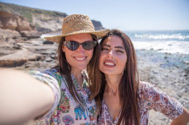 Tatilde olan iki mutlu kız sahilde selfie çeker.