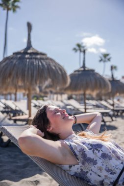 Bir kız tatildeyken kumsalda iskemlede uzanıyor.