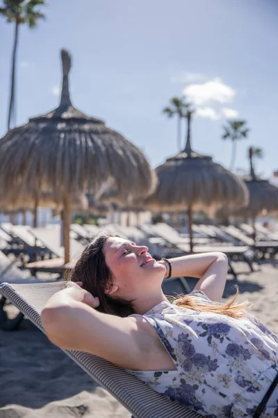 Bir kız tatildeyken kumsalda iskemlede uzanıyor.