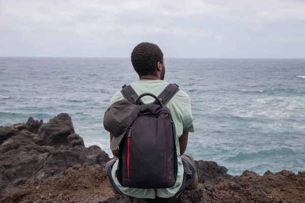 Podróżnik Siedzi Kamieniu Patrzy Ocean Nosi Podróżny Plecak — Zdjęcie stockowe