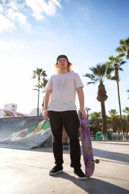 Genç kaykaycı elinde kaykayıyla parkta.