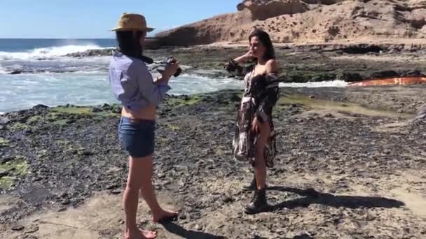 一位摄影师正在拍一个女孩在海滩上摆姿势的照片 现在是夏天 天气很好 两个女孩在海滩上 — 图库视频影像