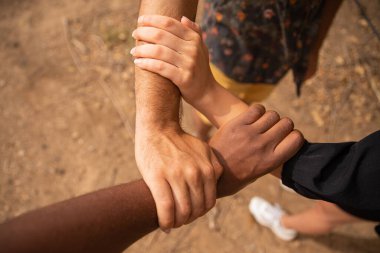 Farklı etnik kökenlere sahip üç el birbirini kavrar ve bir üçgen oluşturur. Çeşitlilik kavramı.