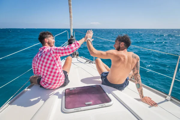 two friends on a boat are happy and do high five, the day is beautiful, the sky is clear and they are enjoying life. Friendship concept.