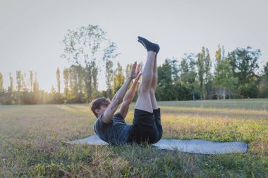 Açık hava parkındaki minder üzerinde vücut egzersizi yaparken bacakları yukarı doğru uzanan adam..