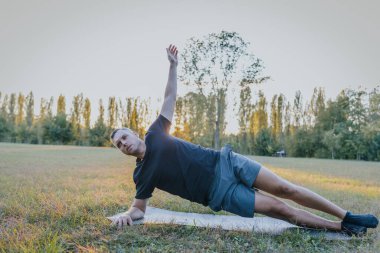 Açık oturum sırasında yoga minderinde yan tahtada dengelenmiş bir adam..