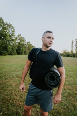 Adam yoga minderi ve sırt çantasıyla dışarı bakıyor..