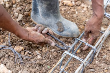 İşçilerin elleri inşaat alanındaki çelik parmaklıklarla teli bağlıyor, beton çubuklarla metal çubuklar örüyor.