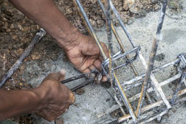 Erkek müteahhit çelik çubuklu metal çubuklar, beton sütunlar örmek için tel örüyor.