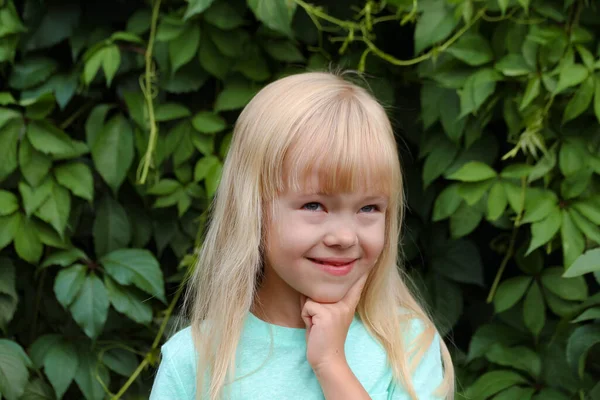 Une petite fille blonde dans un t-shirt à la menthe pense à quelque chose de joyeux ou joyeux, rêves heureux — Photo