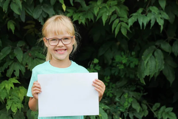 Blonde fille avec des lunettes tenant une feuille de papier vierge avec de l'espace pour le texte — Photo