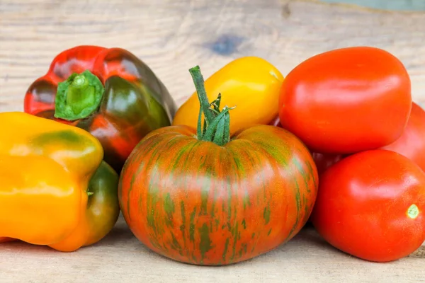 Heldere kleurrijke tomaten en paprika 's van verschillende grootte. Rood, geel, bonte, grote en mini tomaten op een houten ondergrond. — Stockfoto