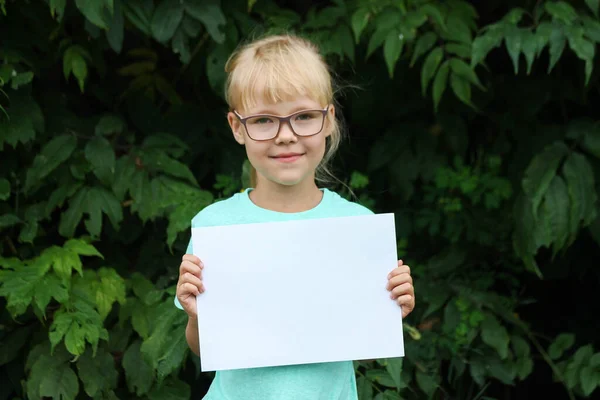Blonde fille avec des lunettes tenant une feuille de papier vierge avec de l'espace pour le texte — Photo