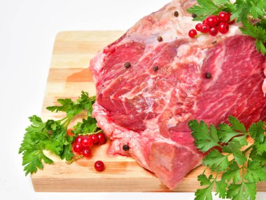 Taze maydanozla süslenmiş tahta kesme tahtasında çiğ et, siyah biber ve kırmızı frenk üzümü. Pişirmeye ve ızgara yapmaya hazır pişmemiş sığır eti taze ve dokusudur..