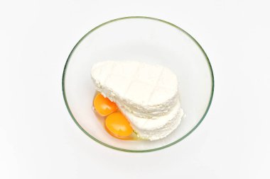 Beyaz arka planda şeffaf cam bir kasede taze süzme peynir ve çiğ yumurta sarısı..