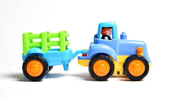 Colorful plastic toy tractor with a detachable trailer and a small driver figure inside the cabin.
