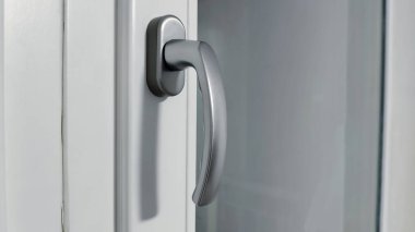 Modern gümüş pencere kulpu beyaz plastik çerçeve yakın görüntüsünde. Modern pencere donanımı ve konut güvenliği özellikleri.