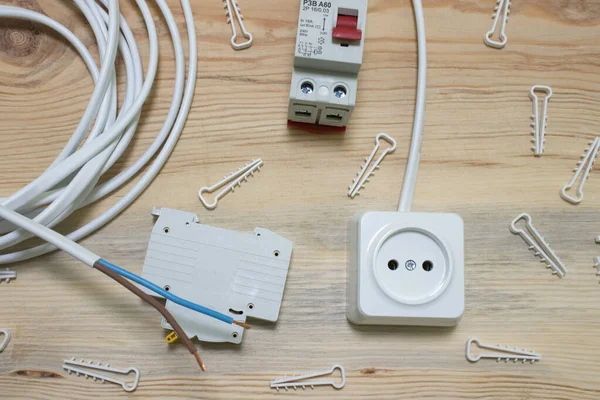Electrical outlet, automatic electrical switch, plastic fasteners for the wire, electrical cable and residual current device on a wooden background close up
