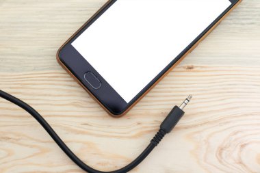 Mobile phone and audio wire on wooden background close up