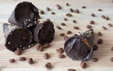 Doldurulmuş çikolata tüpleri ve ahşap masanın üstünde çikolatalı fıstıklar.