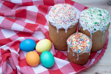 Üç fırında Paskalya pastası, üzerine şeker serpiştirilmiş, dört renkli tavuk yumurtası, kırmızı ve beyaz bir bez, yakın plan.